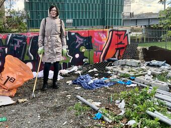 Vergrößerte Ansicht von Eine Frau steht auf dem Platz "ALTER" inmitten von Abfällen, die auf dem Boden liegen.