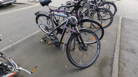 Vergrößerte Ansicht von Dieses Schrottfahrrad ohne Hinterrad belegt einen Fahrradbügel.