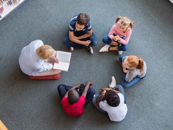 Vergrößerte Ansicht von Eine Erwachsene liest fünf Kindern vor.