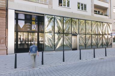 Vergrößerte Ansicht von Eine Frau läuft auf den Eingang eines Museums mit auffälliger Glassfassade zu