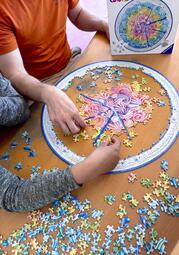 Vergrößerte Ansicht von die Hände von zwei Personen, die auf einem Tisch ein rundes Puzzle legen