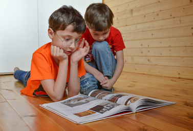 Vergrößerte Ansicht von zwei Kinder sitzen auf dem Boden und schauen sich ein aufgeschlagenes Buch an