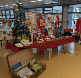 Vergrößerte Ansicht von Tische, Stellwände und ein offener Koffer, die weihnachtlich geschmückt sind. Auf den Tischen und im Koffer liegen Bücher.