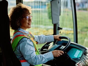 Busfahrerin mit Warnweste sitzt am Steuer