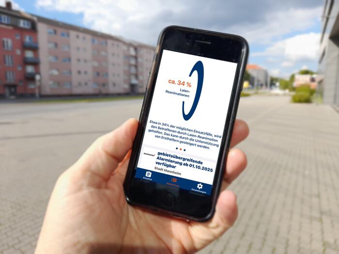 Eine Hand hält ein Handy. Auf dem Bildschirm ist die App Katretter zu sehen. Ein Text besagt, dass die gebietsübergreifende Alarmierung ab 01.10.2025 verfügbar ist